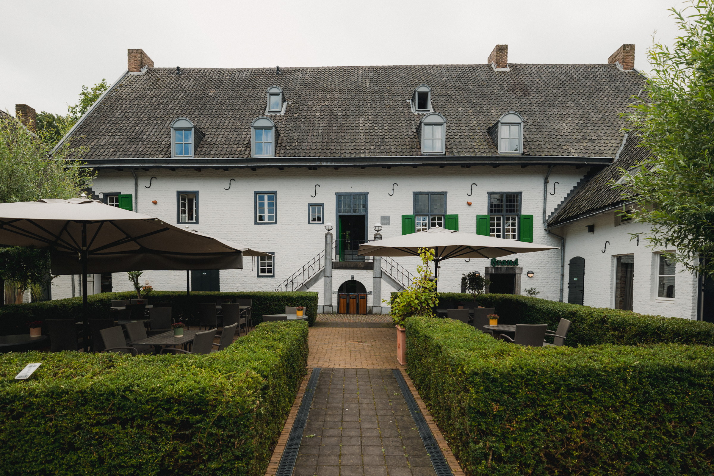 Weiß getünchter Gutshof des Winselerhofs mit grünen Fensterläden, Buchsbaumhecken und Sonnenschirmen im Innenhof