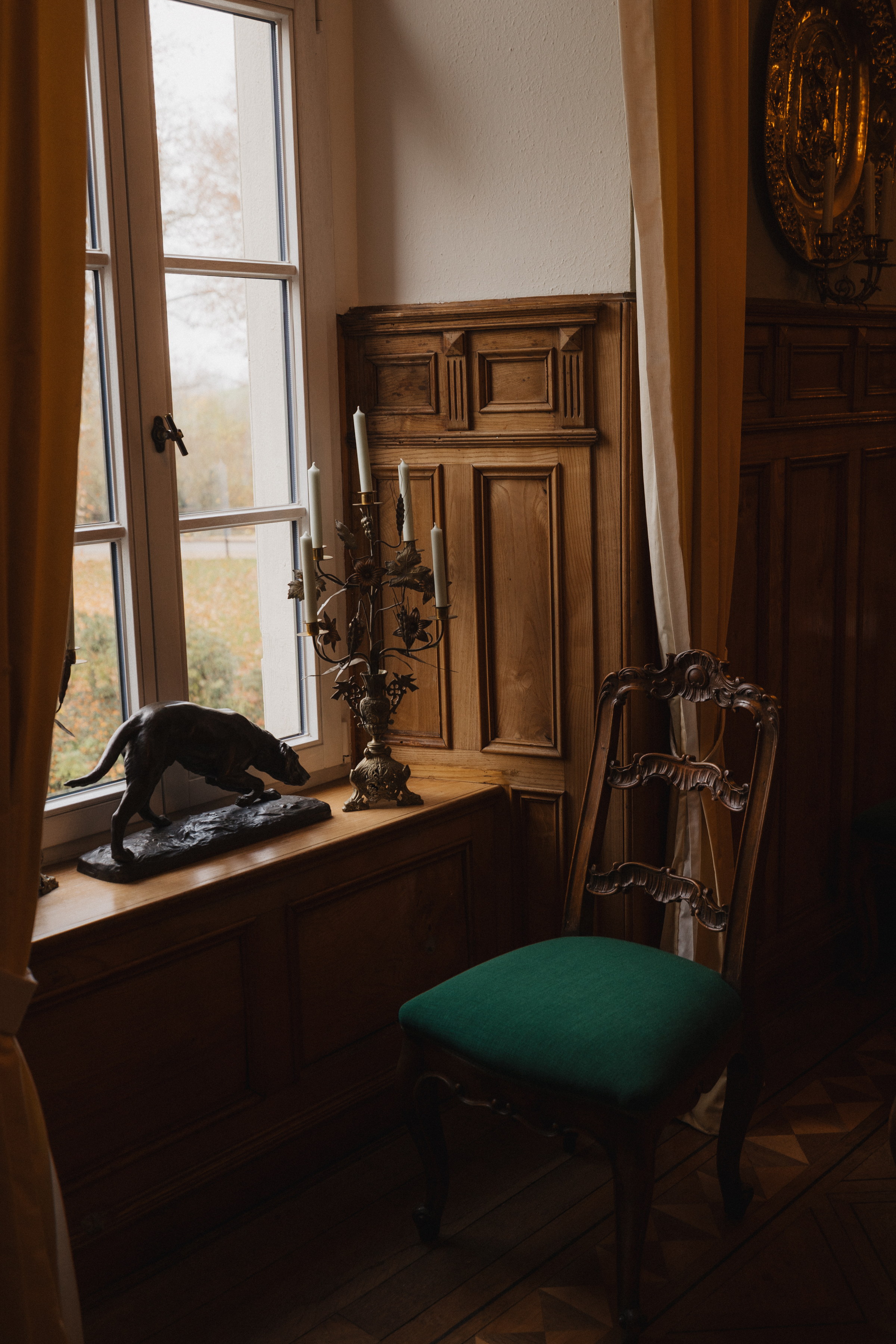 Schwarze Katze auf der Fensterbank neben Kerzenleuchter und grünem Stuhl