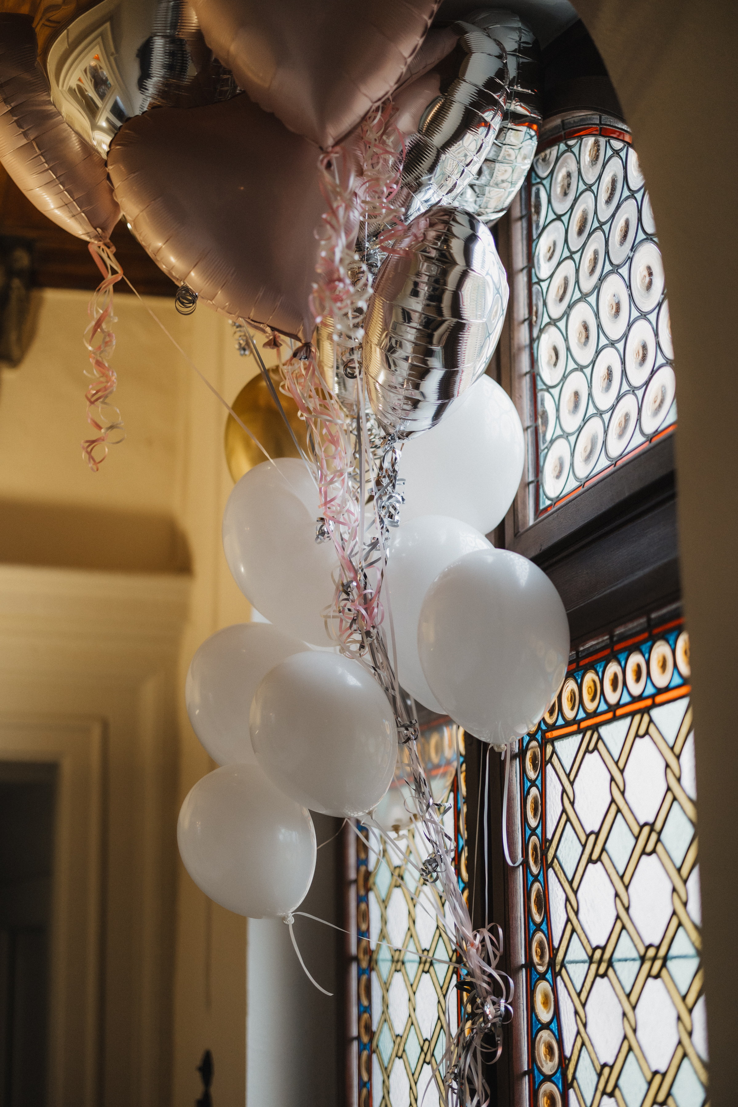 Luftballons in Rosé und Silber vor dem Bleiglasfenster im Treppenhaus der Burg