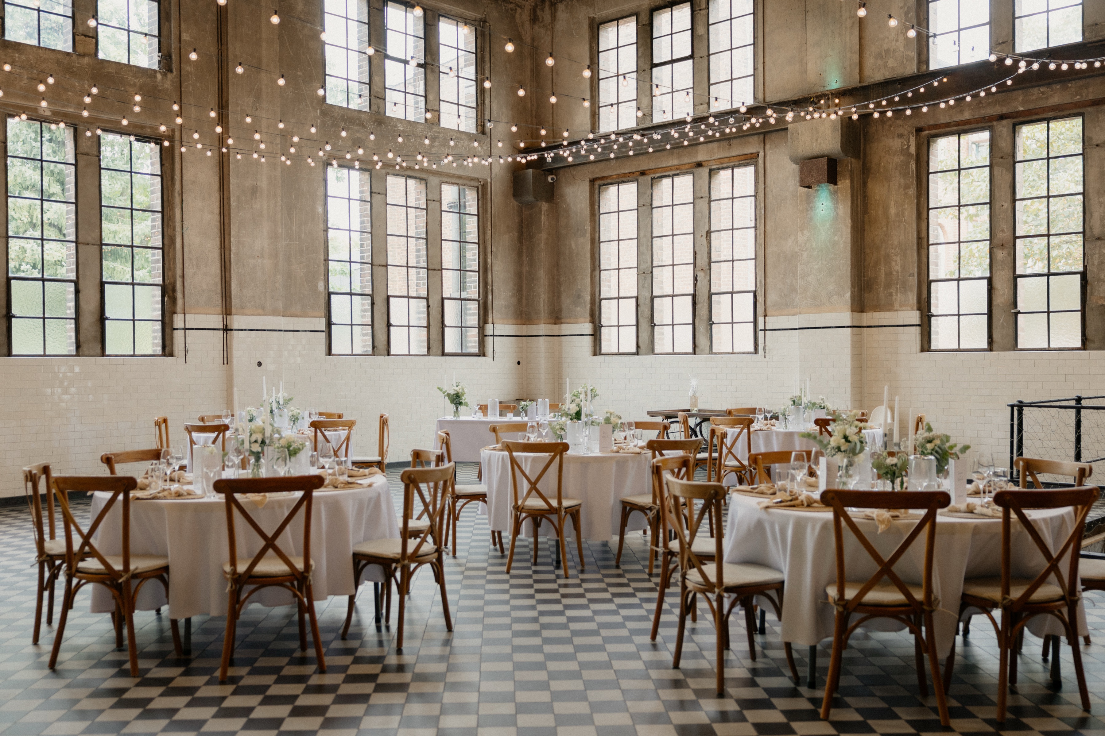 Festsaal der Alten Maschinenhalle mit hohen Industriefenstern, Schachbrettboden und gedeckten runden Tischen
