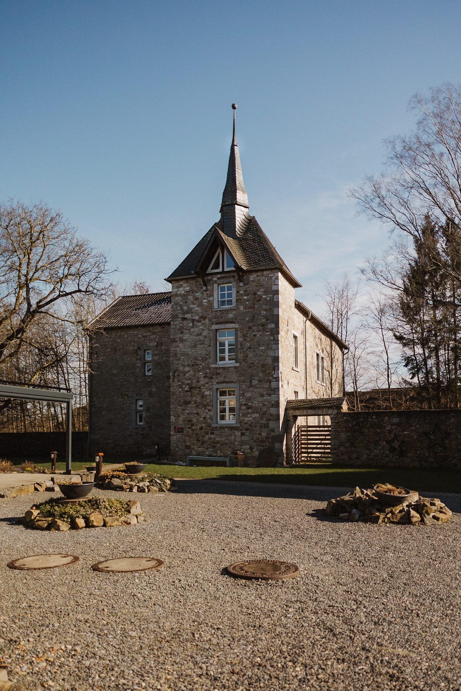 Historisches Gutshaus aus Naturstein mit spitzem Schieferturm, davor ein Kiesplatz