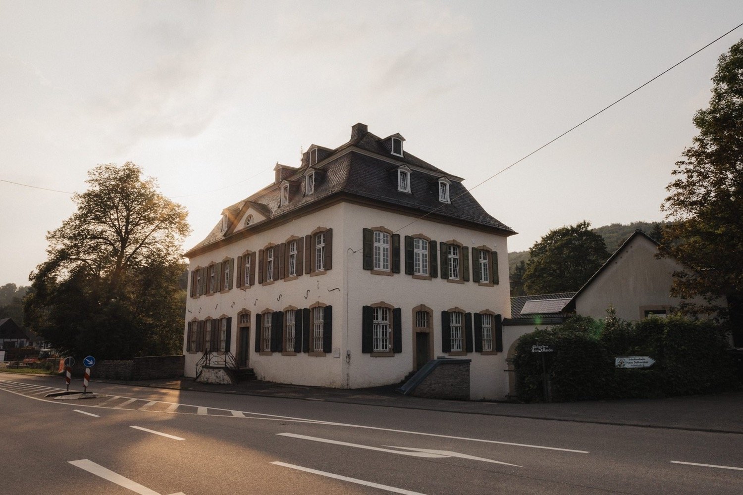 Weißes Herrenhaus mit Schieferdach und grünen Fensterläden an der Straße im Abendlicht