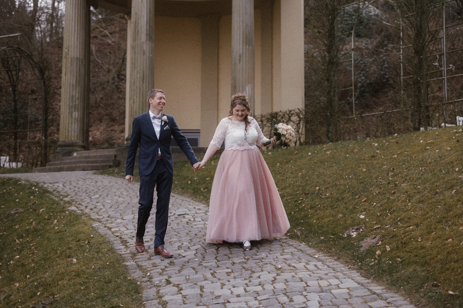 Brautpaar läuft lachend Hand in Hand den Weg herunter