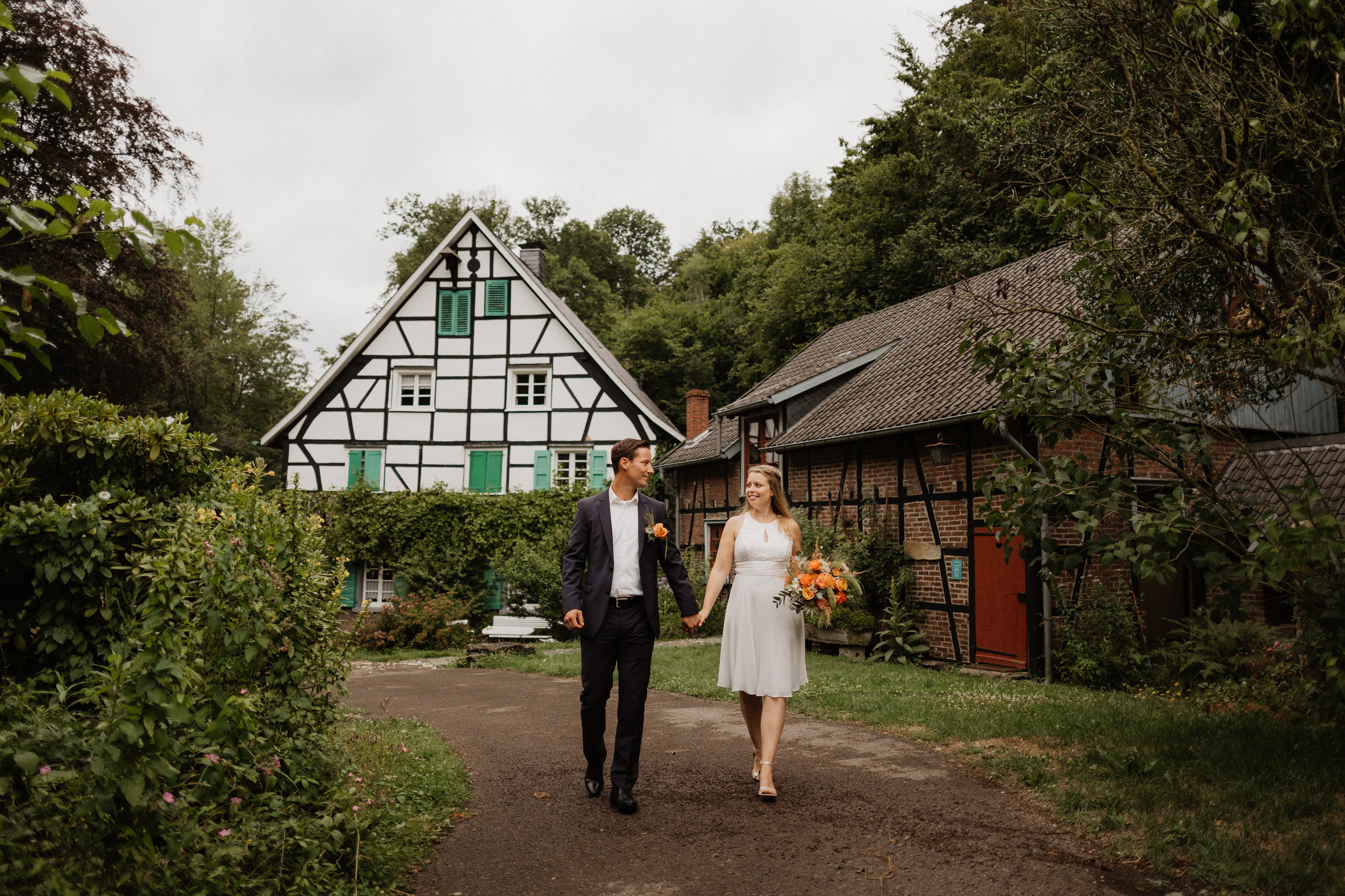 Brautpaar geht Hand in Hand über den Hof der Lambertsmühle, im Hintergrund ein Fachwerkhaus