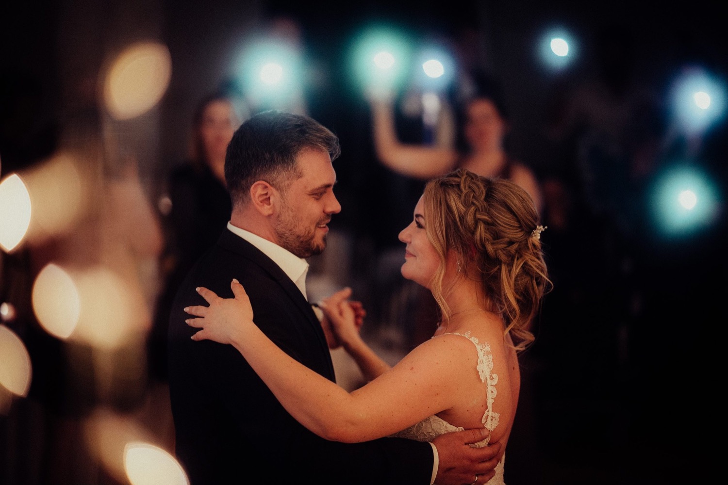 Brautpaar beim Hochzeitstanz, die Gäste stehen im Halbdunkel darum herum
