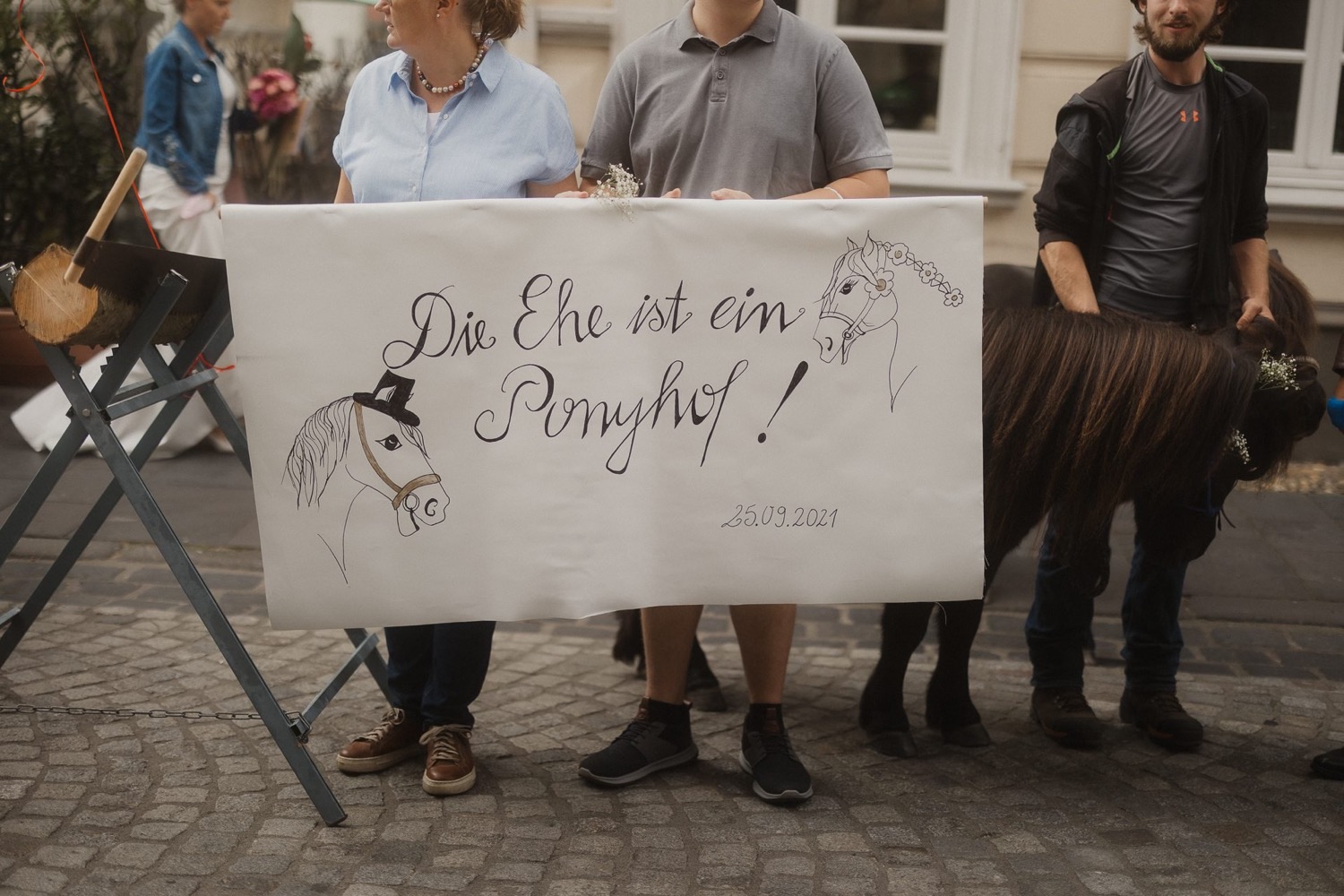 Gäste halten ein Banner mit der Aufschrift „Die Ehe ist ein Ponyhof“, daneben ein Esel