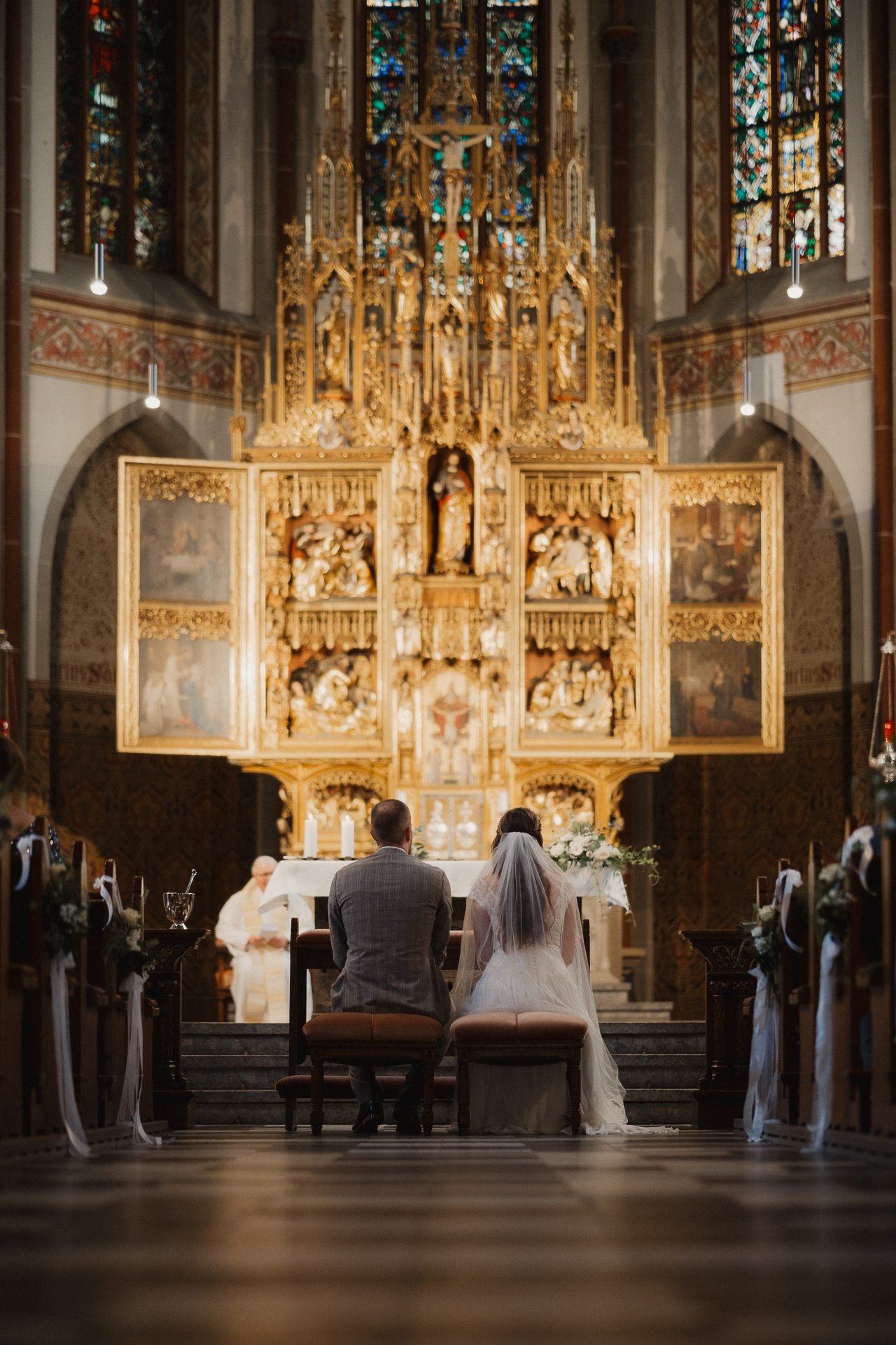 Blick durch das Kirchenschiff auf den goldenen Altar, davor das Brautpaar