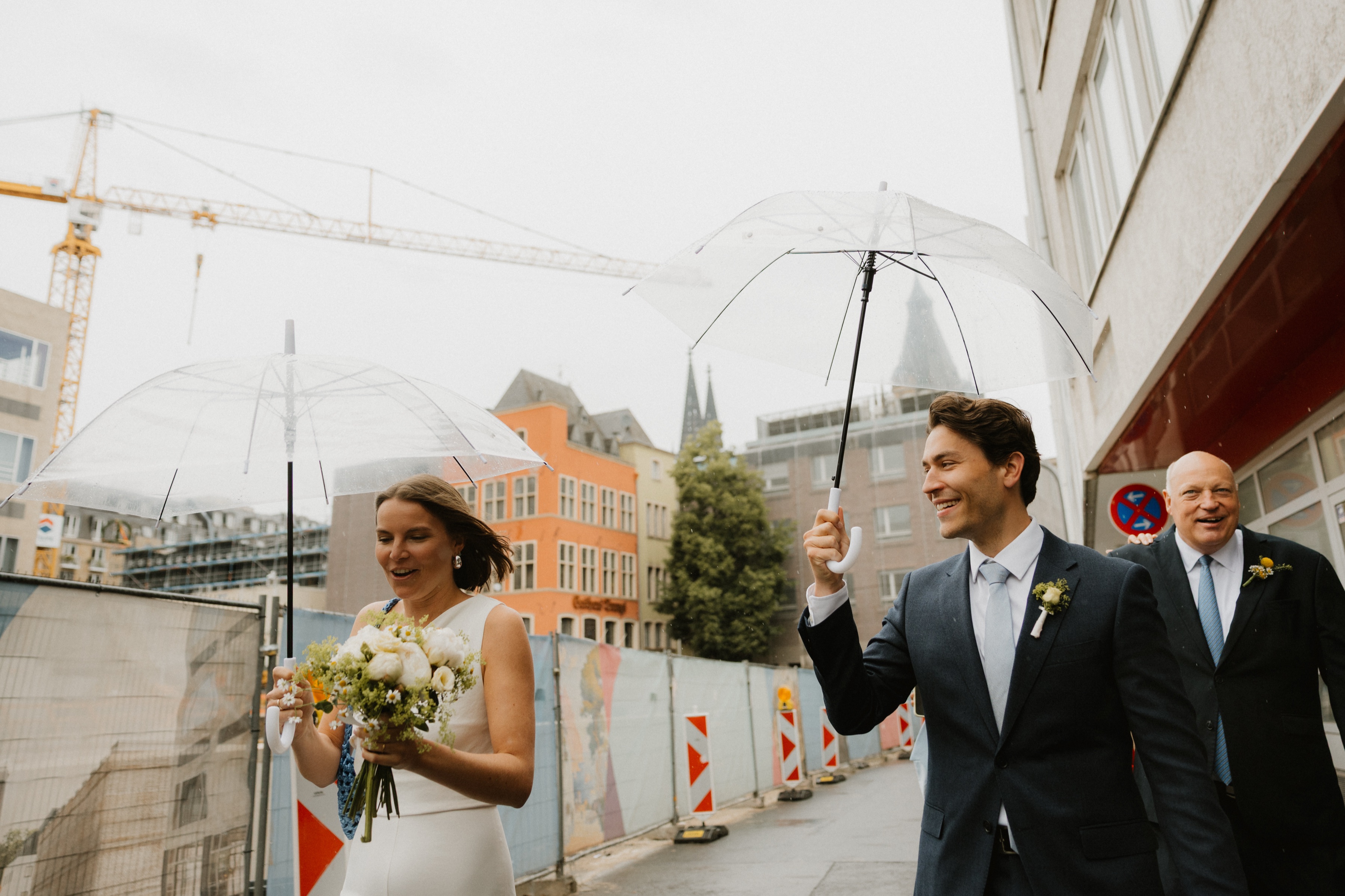 Brautpaar mit Regenschirmen auf dem Weg durch die Kölner Innenstadt, Domspitzen im Hintergrund