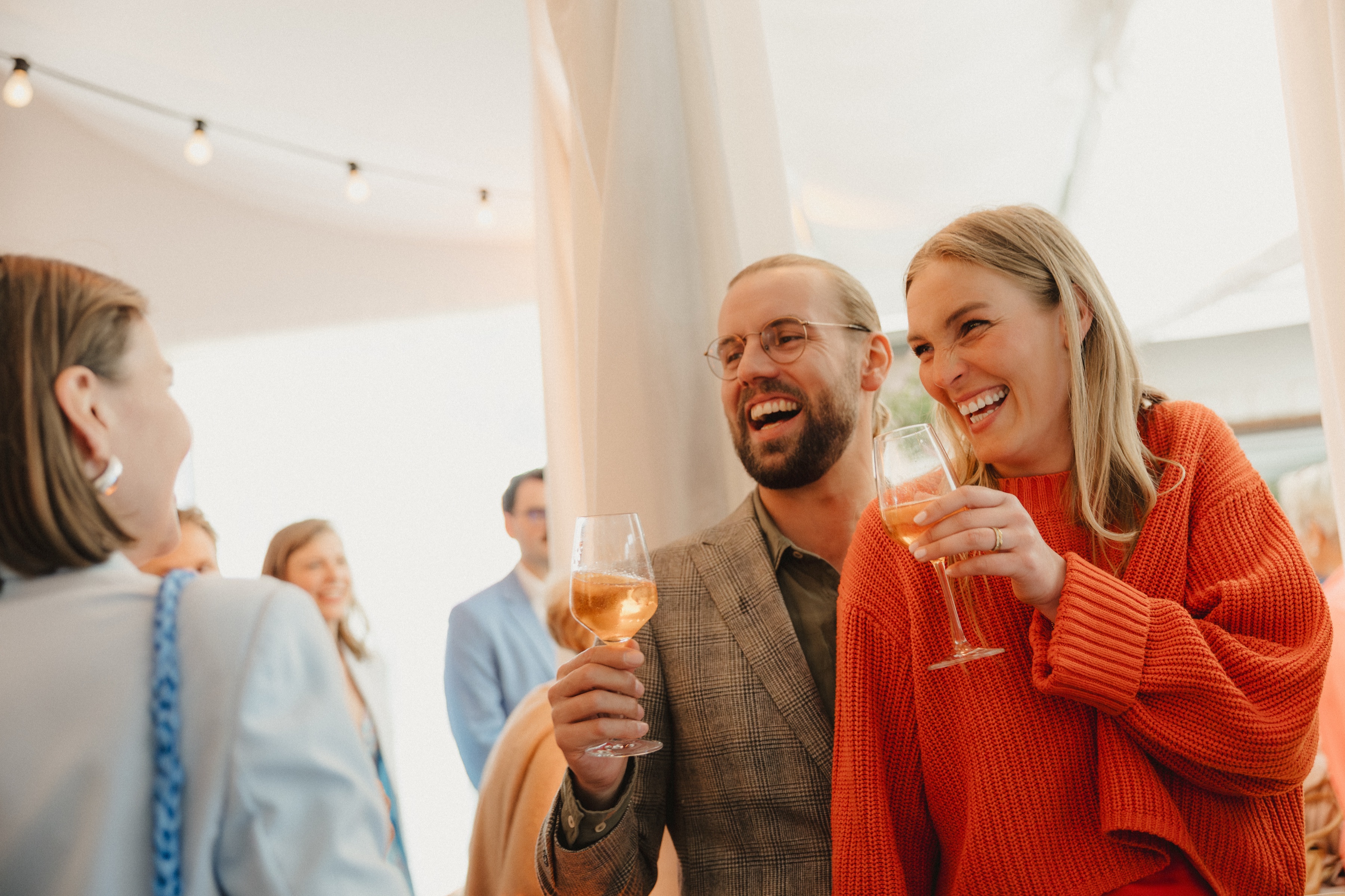 Gäste stoßen im Zelt lachend mit Wein an