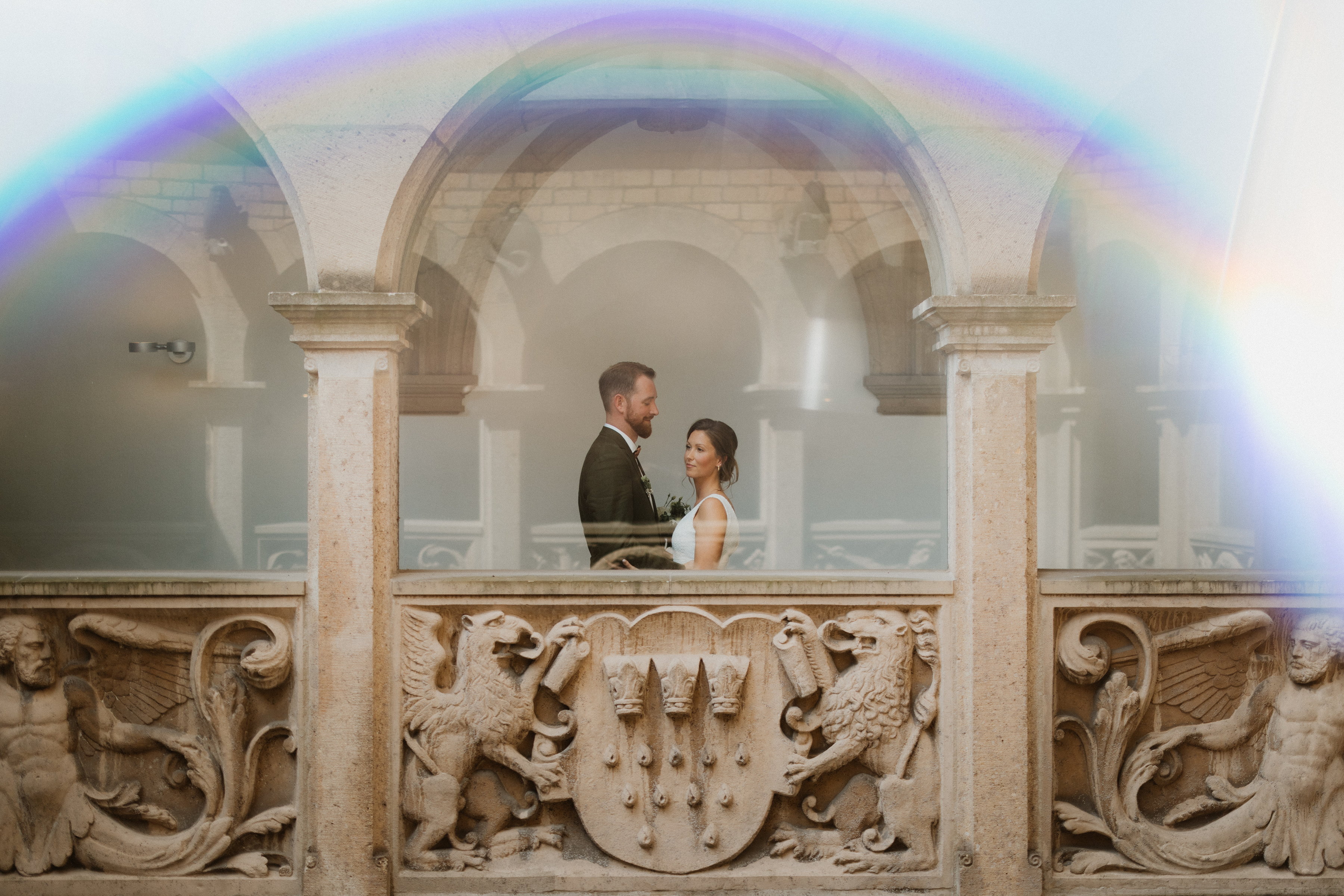 Brautpaar steht sich in der Rathauslaube gegenüber, ein Regenbogen-Lichtreflex spannt sich über das Bild