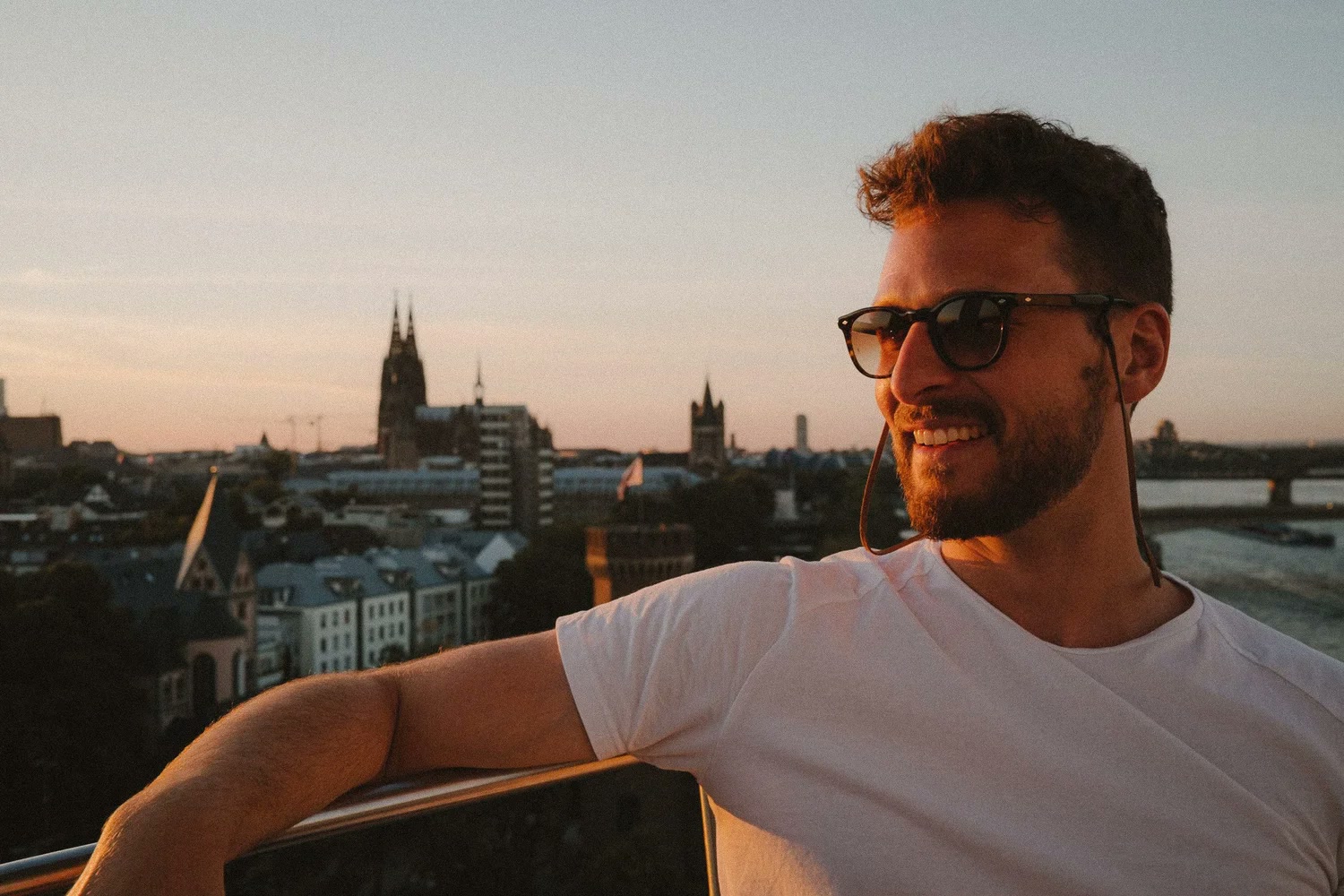 Fabian Rudolf an einem Geländer über Köln, dahinter die Türme der Altstadt im Abendlicht